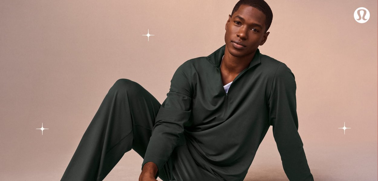 Pullover verde scuro con cerniera, realizzato in tessuto morbido, caratterizzato da un colletto alto e un design leggero. Il modello indossa un berretto leggero e una maglietta bianca sotto.