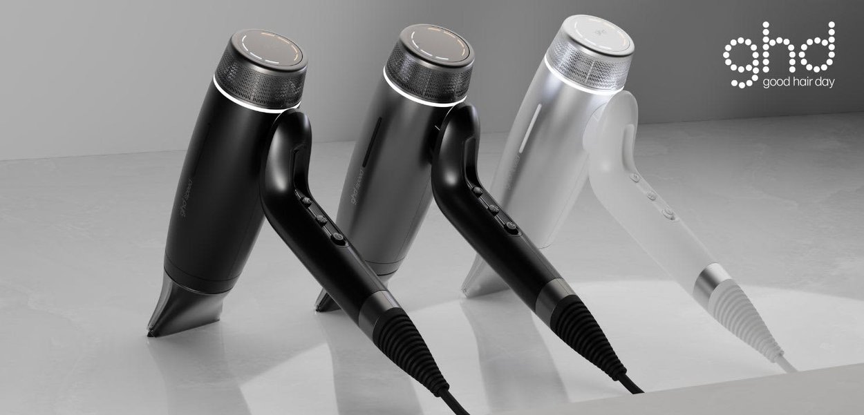 Drie strakke föhns in zwart, donkergrijs en wit, rechtop uitgelijnd op een reflecterend oppervlak met het ghd-logo in de hoek.