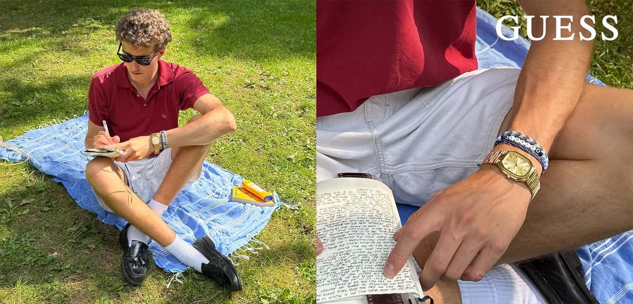 Rode polohemd, witte shorts en zwarte schoenen. Zittend op een blauwe deken schrijft hij in een notitieboek met een gouden horloge en een patroonsband.