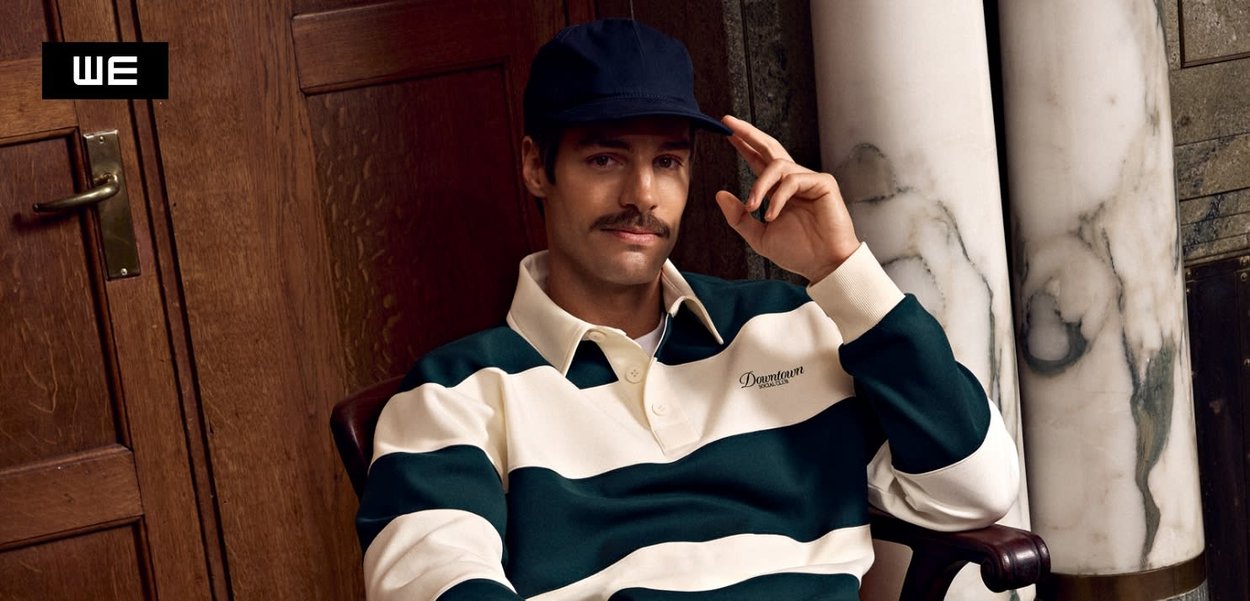 Weiß-grün gestreiftes Rugby-Shirt mit Kragen, getragen mit einer dunkelblauen Mütze. Auffällige Details sind das gestickte "Downtown"-Logo auf der Brust.