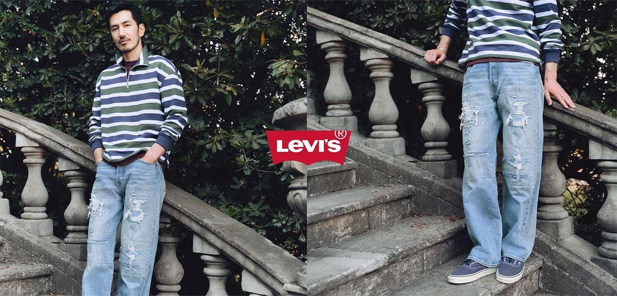 Man met gestreepte trui en gescheurde jeans, staand op stenen trap met balustrade buiten, Levi's-logo gecentreerd tussen twee uitzichten.