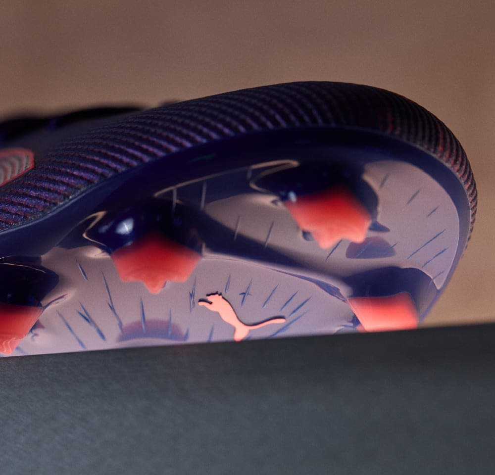 Lila strukturierte Fußballschuhsohle mit rosa Akzenten und konischen Stollen. Besitzt ein sichtbares Markenlogo und eine glatte, reflektierende Oberfläche.