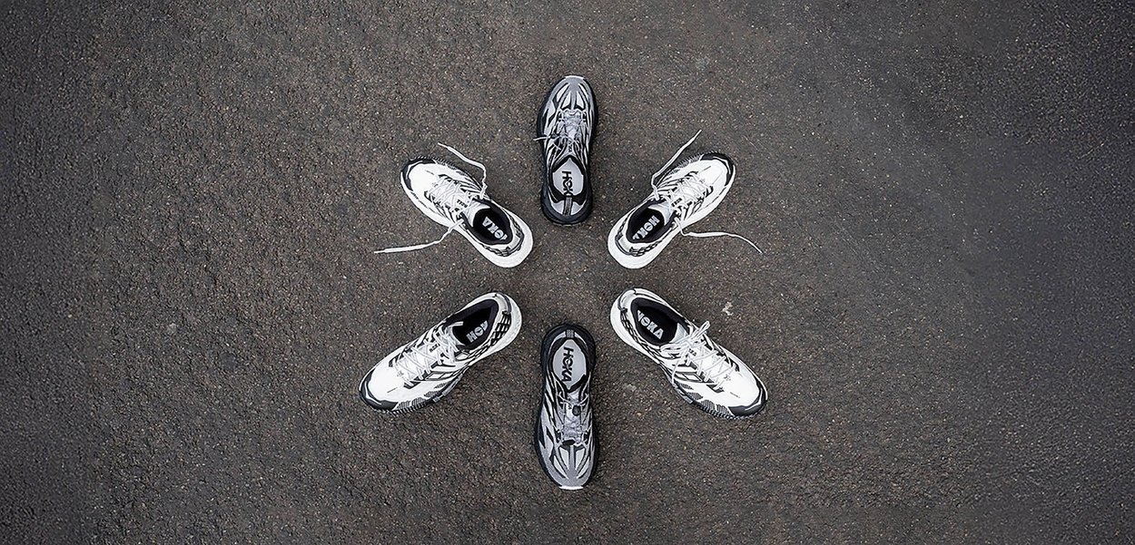 Six pairs of running shoes in black and white, featuring mesh material, textured soles, and contrasting accents, arranged in a circular pattern.