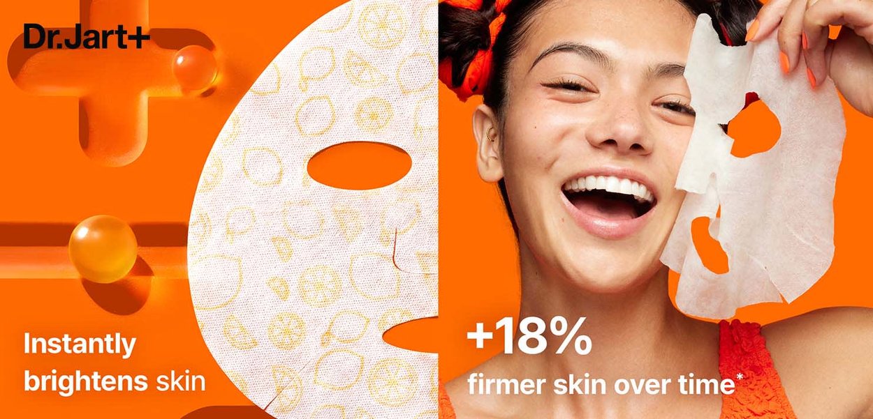 Hvit ansiktsmaske med sitrusmønster, livlig oransje bakgrunn, modell som holder masken, viser klar hud, smilende, uformell bekledning.
