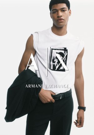 Weißes ärmelloses T-Shirt mit grafischem Druck, kombiniert mit schwarzen Hosen und einer schwarzen Jacke, die über einem Arm hängt. Einfacher Gürtel und Uhr.