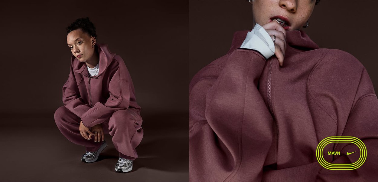 Persoon in mauve trainingspak en sneakers die hurkt op een bruine vloer, close-up van de met rits sluitende kraag van het jack met de hand dicht bij de mond.