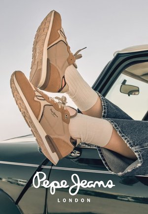 Piernas con calcetines blancos y zapatillas marrones apoyadas en la puerta de un coche vintage negro, con el logo "Pepe Jeans London" abajo.