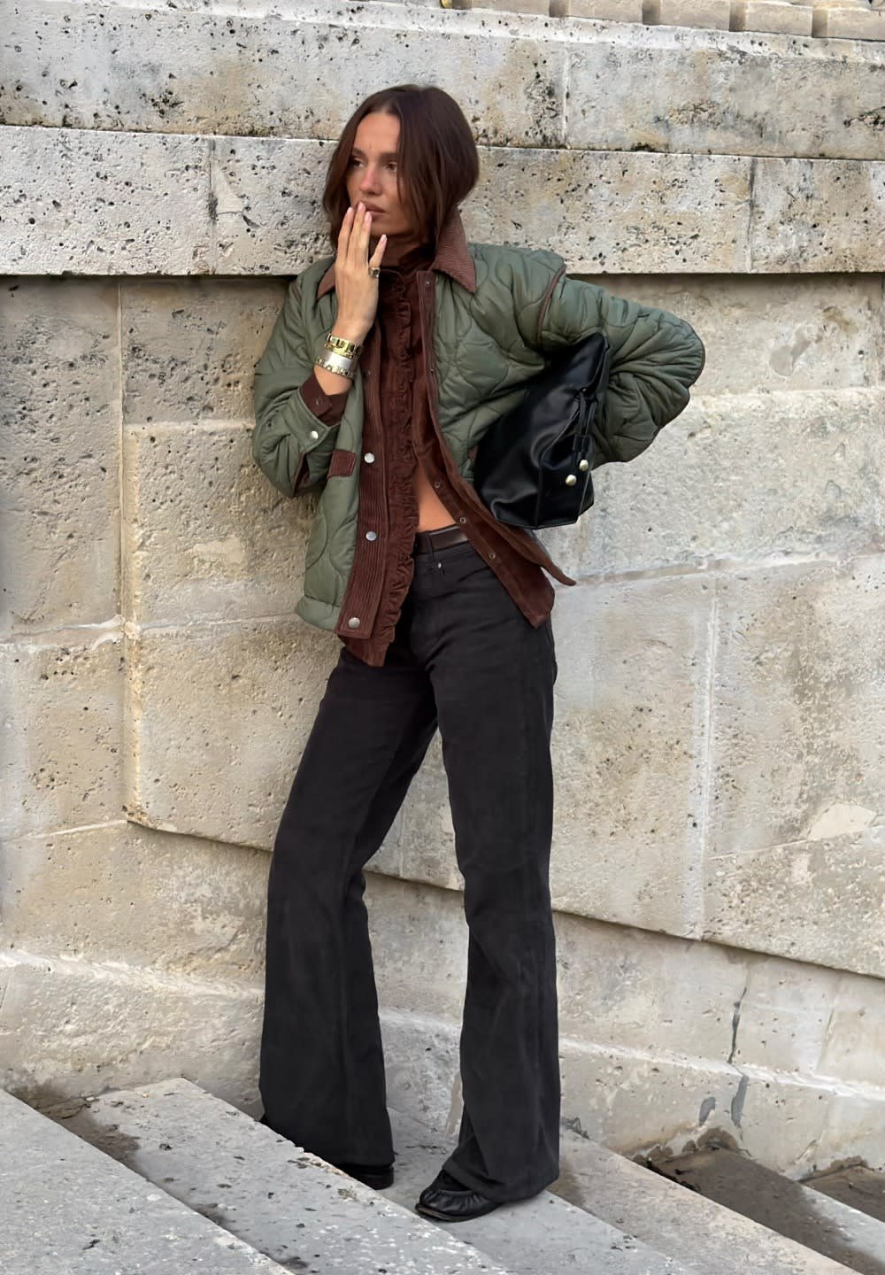 Chaqueta verde acolchada con cuello de pana marrón, combinada con una camisa marrón y pantalones negros acampanados. Bolso negro y pulseras plateadas.
