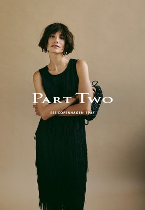 Abito nero con frange, senza maniche, dalla texture liscia e dalla vestibilità comoda. Abbinato a una borsa intrecciata. Sfondo neutro.