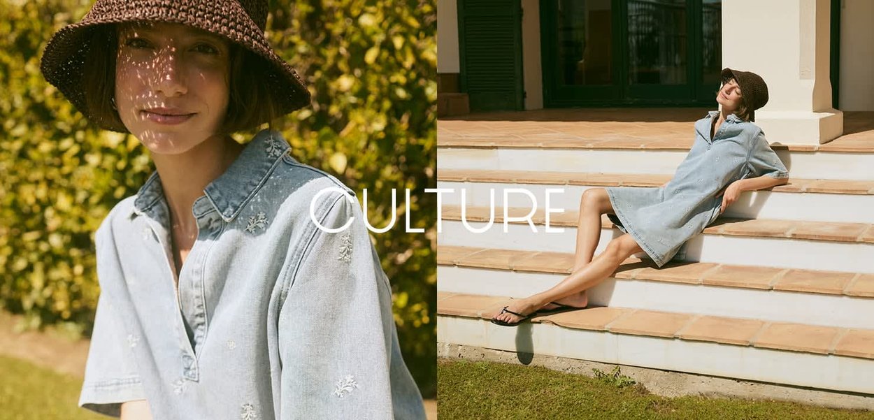 Femme portant une robe en denim clair et un chapeau bob marron, assise en plein air sur de l'herbe et des marches dans un jardin ensoleillé.