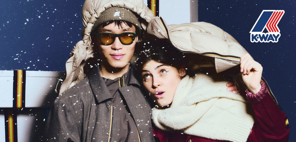 Dos personas llevan ropa de abrigo. Una lleva una chaqueta acolchada beige y un gorro verde, la otra lleva una bufanda blanca y un suéter granate.