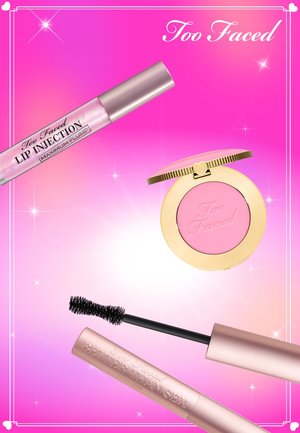 Too Faced producten: een transparante lipgloss met roze accenten, een ronde roze blushcompact met gouden rand, en een zwarte mascaraborstel.