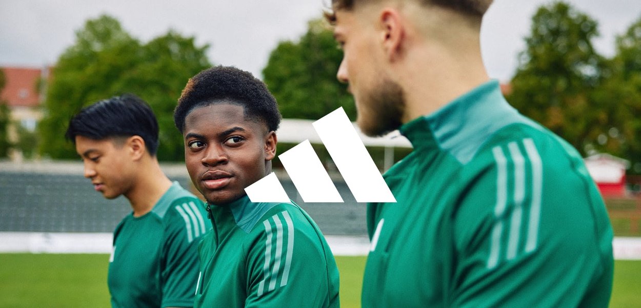 Vestes de sport vertes avec des rayures blanches, portées par trois personnes sur un terrain de sport ; logo affiché de manière proéminente au centre.