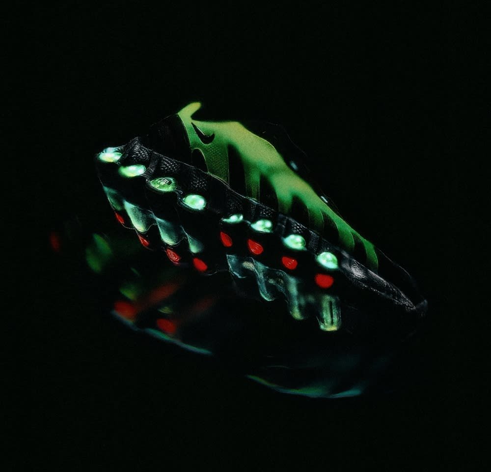 Zwarte en groene sneaker met een uniek golvend ontwerp, met verlichte groene en rode accenten op de zool en gestructureerde materialen.