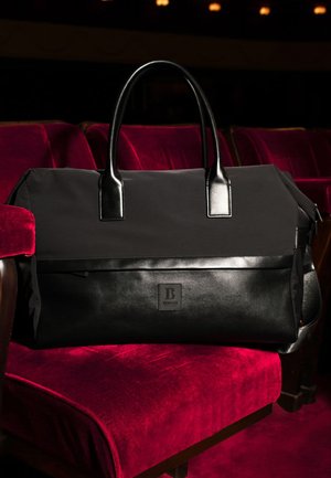 Ampia borsa da viaggio nera in nylon con dettagli in pelle. Dotata di due manici e di un logo a toppa sul davanti. Finitura strutturata.