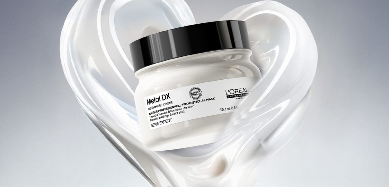 L'Oréal Metal DX Haarmaske im Glas mit schwarzem Deckel, umgeben von einer weißen cremigen Spirale, die auf hellem Hintergrund eine Herzform bildet.