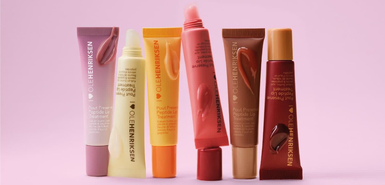 Sei tubetti di trattamento labbra Ole Henriksen in vari colori con campioni di prodotto su uno sfondo rosa.