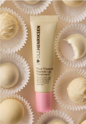 Traitement des lèvres au peptide dans un tube beige clair avec un capuchon rose, entouré de truffes en chocolat blanc dans des caissettes à cupcake.
