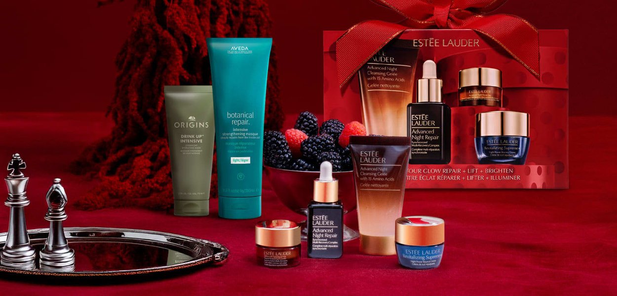 Estee Lauder huidverzorgingsset in een rode doos met een strik, met verschillende formaten donkere en lichte flessen, een groene tube en een zilveren plateau.