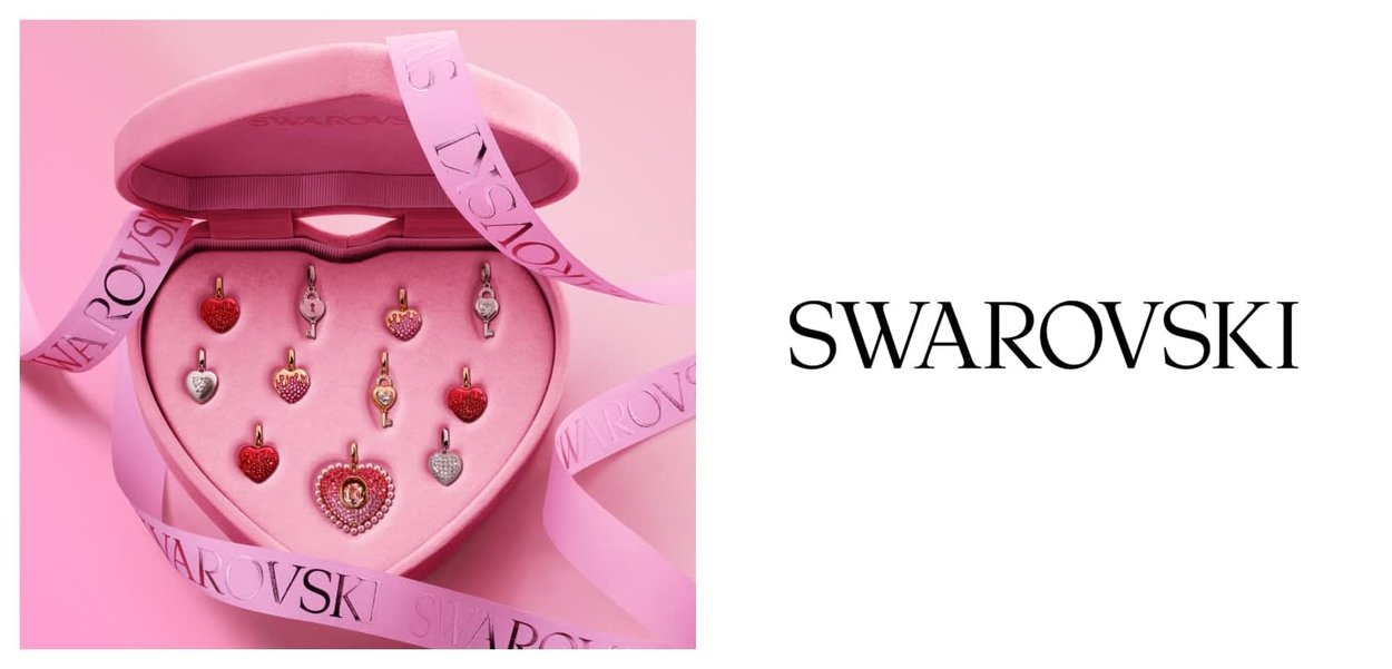 Boîte en forme de cœur contenant des breloques en cristaux Swarovski rouges, roses et argent disposées à l'intérieur sur un fond rose.