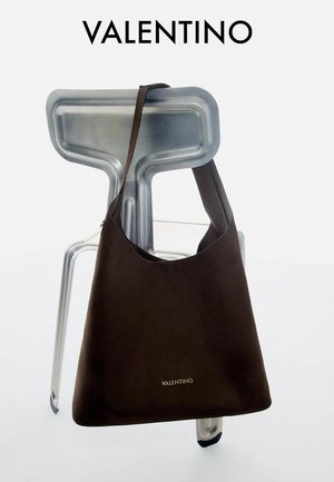 Donkerbruine Valentino leren schoudertas hangend aan een moderne metalen stoel, merknaam in goud op de voorkant van de tas.