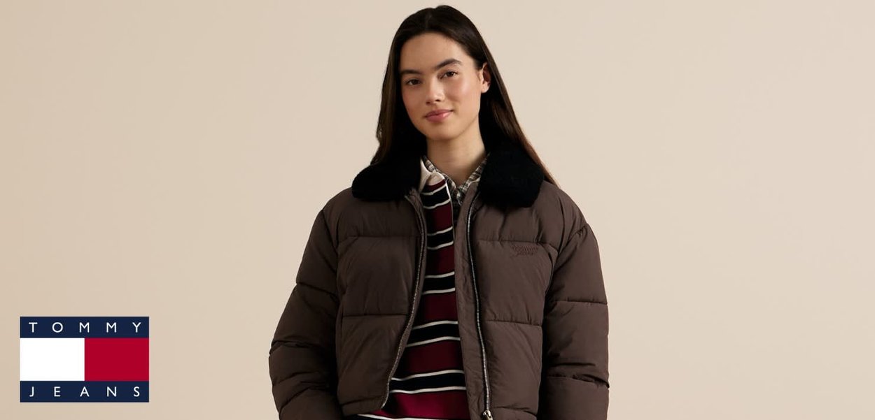 Veste matelassée marron avec col noir, fermeture éclair et design matelassé, portée sur une chemise rayée. Logo en bas à gauche.