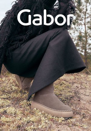 Gabor enkellaarsjes in taupe suède met een dikke, gestructureerde zool en gestikte details. Draag ze met een donker, franjes outfit op natuurlijke ondergrond.