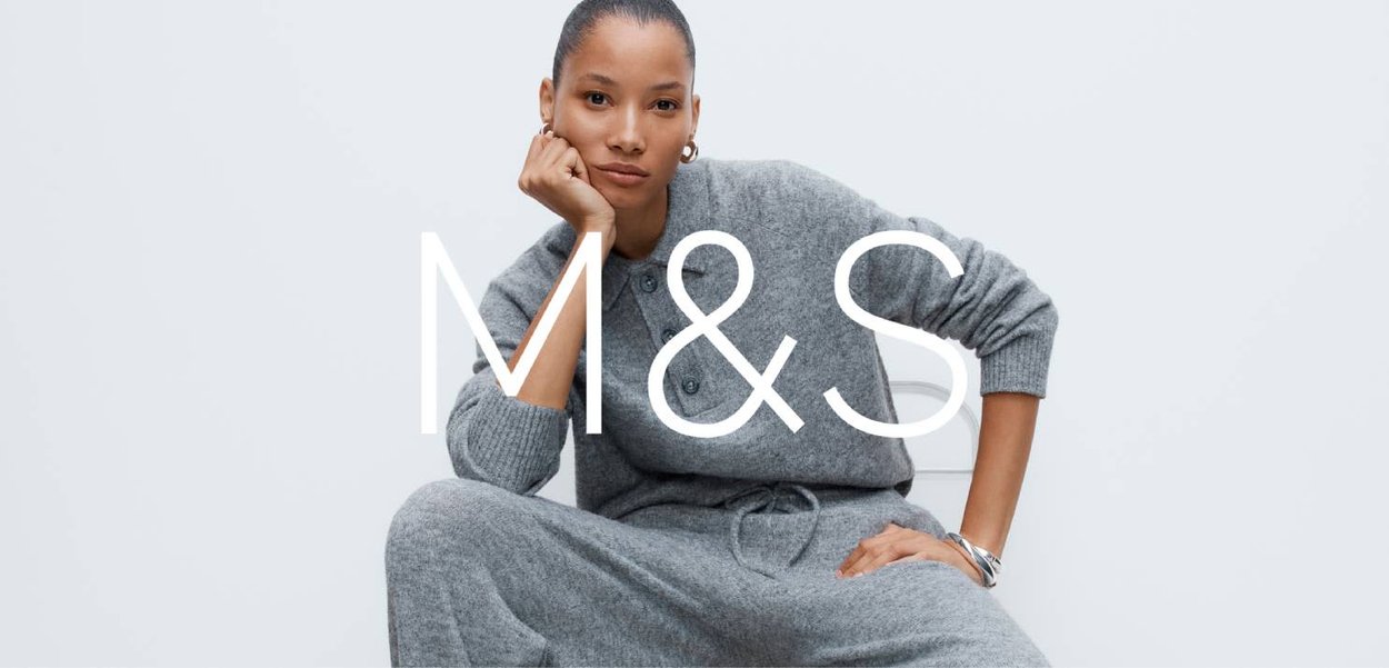 Szara dzianinowa odzież domowa z kołnierzem zapinanym na guziki i ściągaczem w pasie. Modelka siedzi, prezentując miękką fakturę i swobodny design.