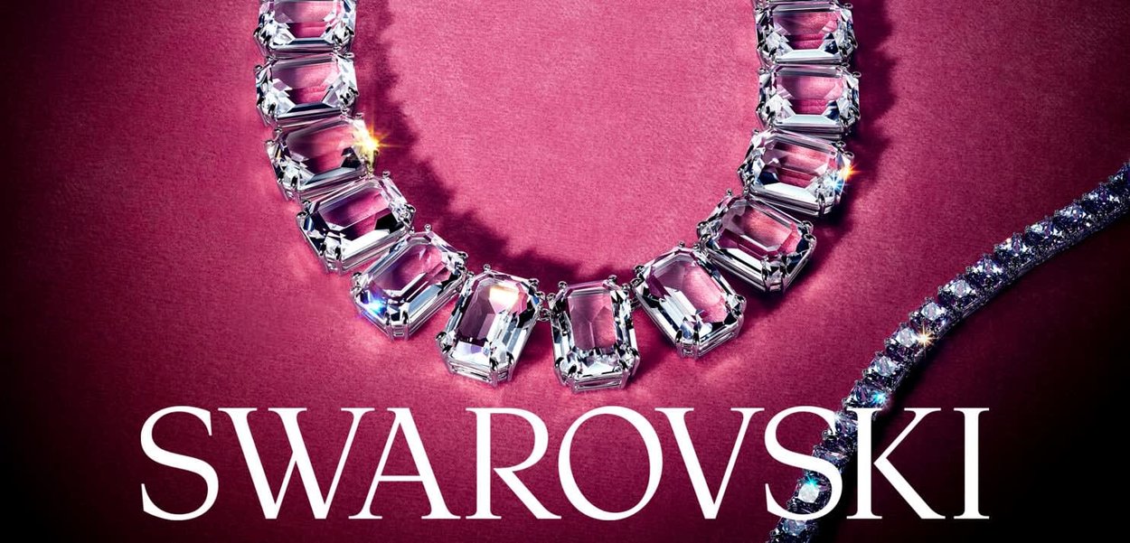 Kristallen ketting met rechthoekig geslepen stenen, gezet in zilverkleurige hardware, op een textuur achtergrond in roze; inclusief de merknaam "Swarovski."