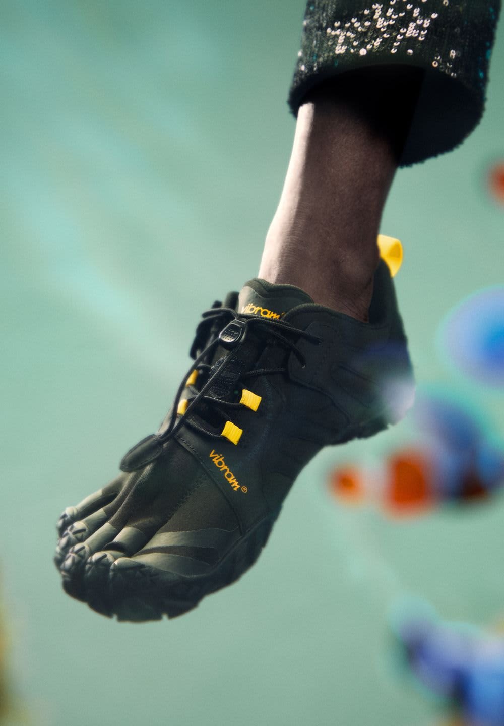 Black five-toed shoe with Vibram® sole, featuring yellow laces and accents. Textured upper with a snug fit, suitable for various activities.