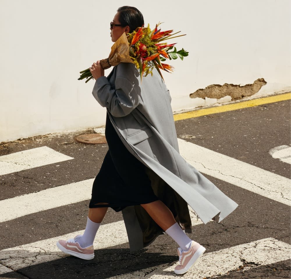 Siv plašč preko črne obleke, bele nogavice in roza superge. Nosila je šopek pisanih rož in hodila po prehodu za pešce.