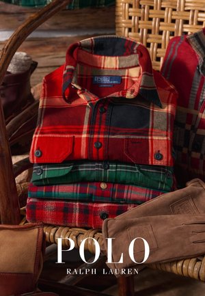 Camicie di flanella a quadri impilate in rosso, verde e nero con dettagli a bottoni, accanto a guanti marroni, su una superficie di cesto intrecciato.