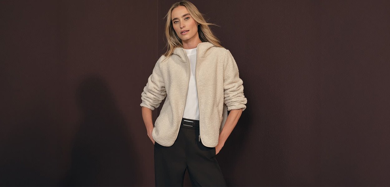 Crème-kleurig fleecejack met een hoge kraag, ritssluiting en geribde manchetten, gedragen over een witte shirt en zwarte broek.