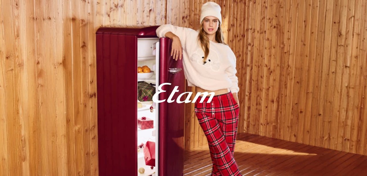 Frigorifero retrò rosso, finitura lucida, bordi arrotondati, porta aperta che mostra della frutta. Parete e pavimento in legno, figura femminile con maglione chiaro e pantaloni a quadri.