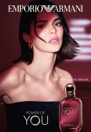Frau mit kurzen dunklen Haaren, die goldene Ohrringe und ein schwarzes Oberteil trägt, neben einer pinkfarbenen Parfümflasche mit der Aufschrift "Power of You" von Emporio Armani.