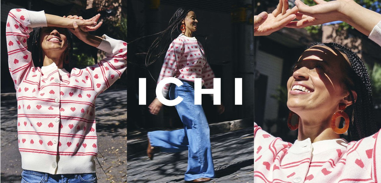 Frau mit geflochtenem Haar, die einen weißen Pullover mit roten Herzen und blaue Jeans trägt, lächelt und bewegt sich bei sonnigem Wetter im Freien.