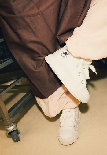 Zapatillas de lona blancas con punta redonda, suela de goma y cordones con ojales. Presentan un logo "Converse All Star" en blanco y negro.