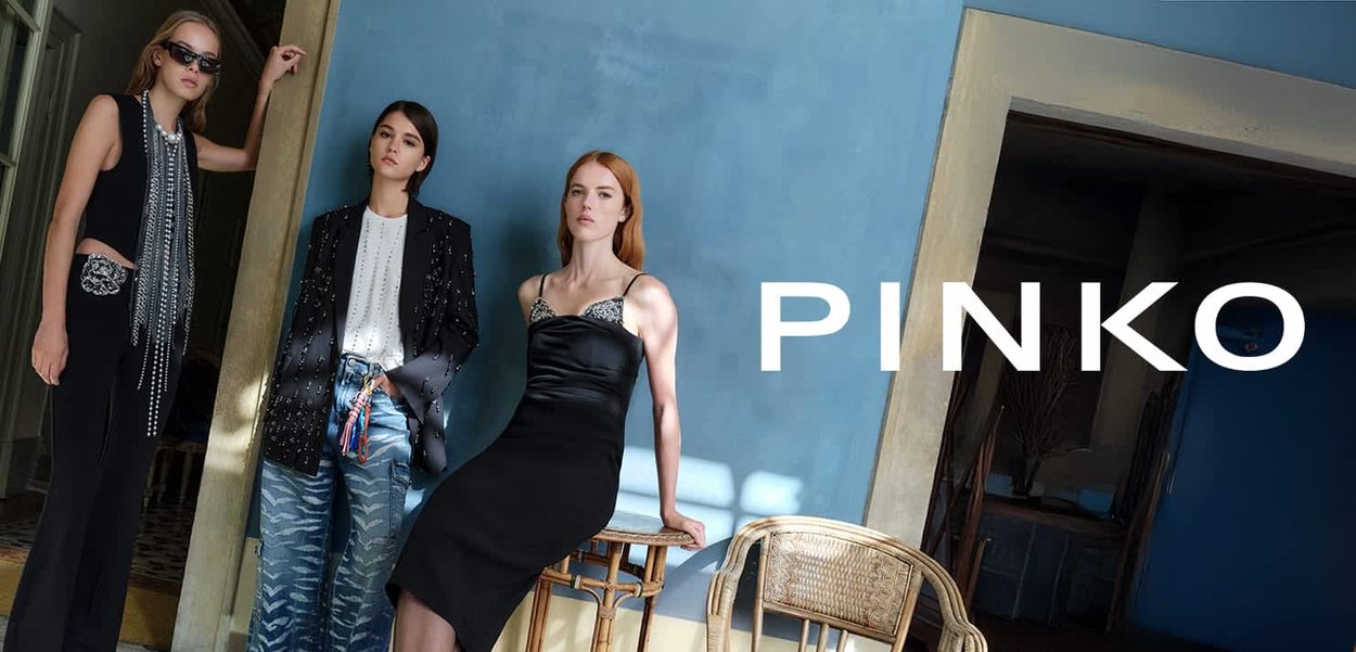 Tre modelle mostrano la moda. Una indossa un vestito di raso nero con dettagli argento, un'altra una giacca nera di paillettes e jeans con motivo, e la terza una canottiera con dettagli a frange.