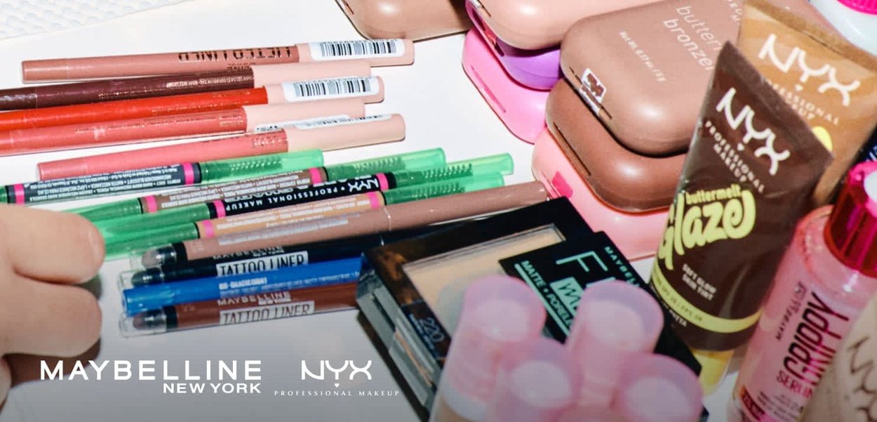Varietà di prodotti per il trucco tra cui matite per labbra, eyeliner, fondotinta, bronzer e illuminante liquido disposti su una superficie bianca.