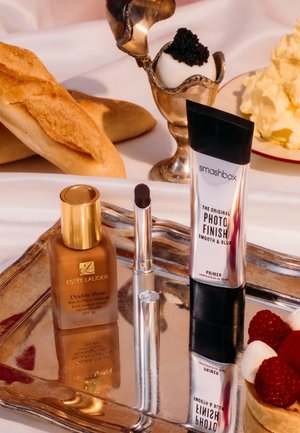 Bouteille en verre marron avec bouchon doré, tube argenté et rouge à lèvres foncé sur un plateau argenté accompagné de pain, un dessert garni de caviar et du beurre fouetté.