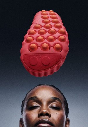 Outil de massage en caoutchouc rouge avec une surface texturée, présentant des nodules circulaires en relief et une forme arrondie, conçu pour une prise en main et un confort optimaux.