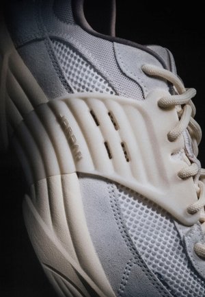 Gros plan sur une chaussure de sport gris clair avec des panneaux en filet et en daim, une semelle épaisse sculptée, des lacets et le logo "JORDAN" sur le côté.