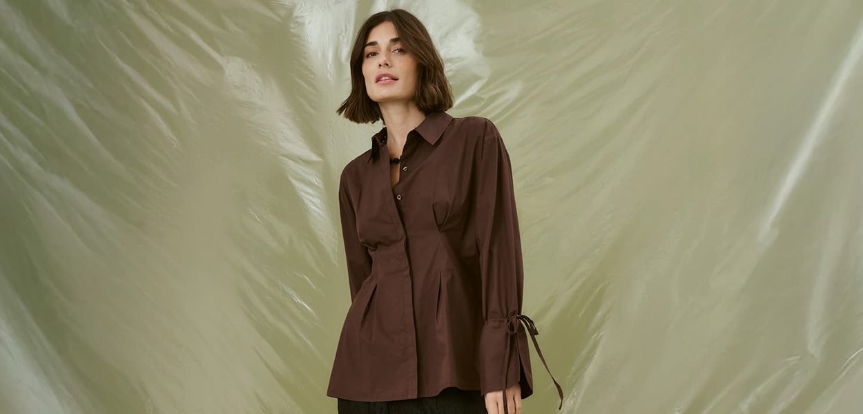 Brown long-sleeve button-up shirt with a fitted bodice, pleated detail, and tie accents at the wrists. Smooth texture against a light background.