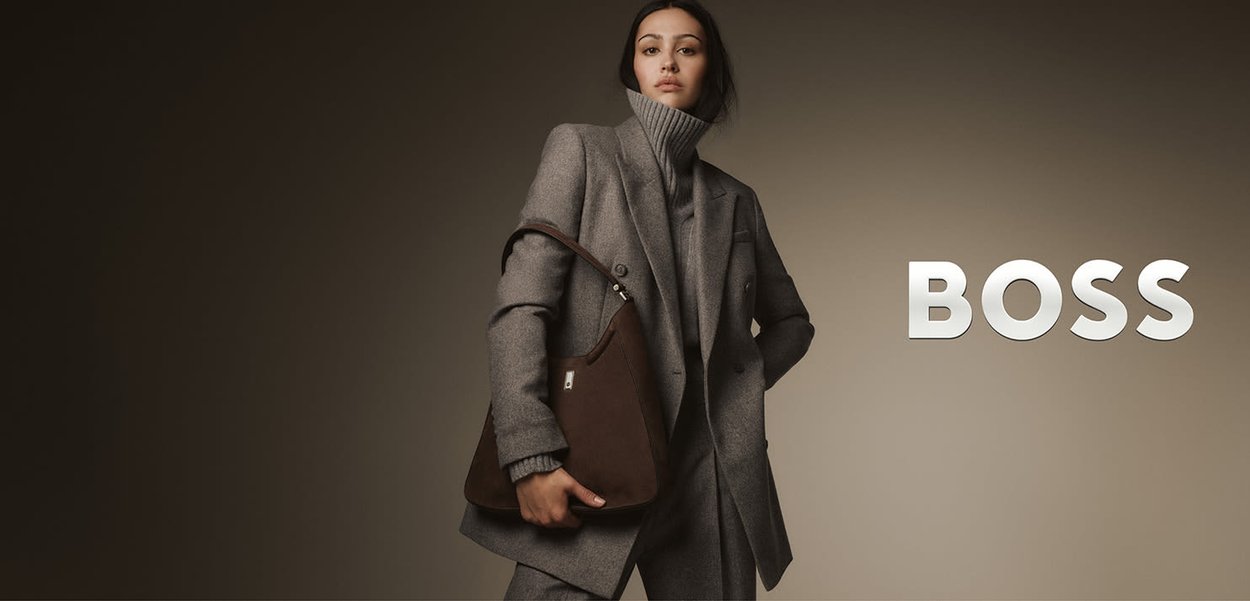 Grijze wollen blazer gedragen over een grijze coltrui, gecombineerd met een bruine leren schoudertas met verstelbare riem en een metalen accent.