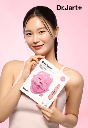 Pink Cryo Rubber facial mask pack featuring a sculpted face design. The product is held by a person in a light-colored top against a pink backdrop.