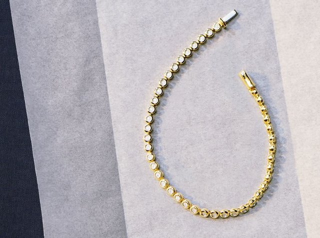 Χρυσό βραχιόλι με κυκλικούς συνδέσμους διακοσμημένους με διαφανείς πολύτιμες πέτρες, τονίζοντας την ομαλή μεταλλική του επιφάνεια και μια διακριτική λάμψη.