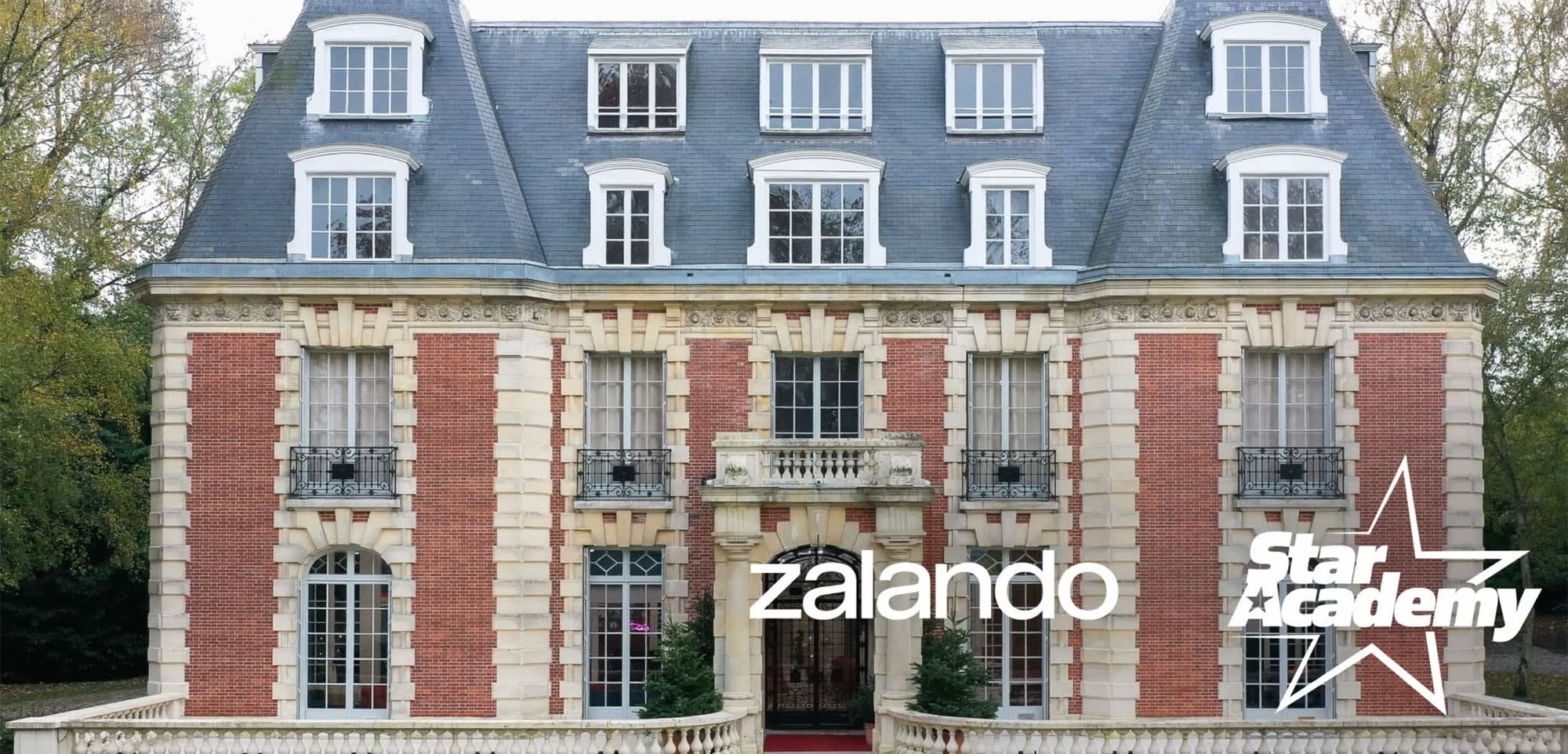 Bâtiment en briques avec des encadrements de fenêtres blancs, un toit en ardoise grise, des accents décoratifs en pierre et des balcons en métal. Logos de Zalando et de Star Academy en superposition.
