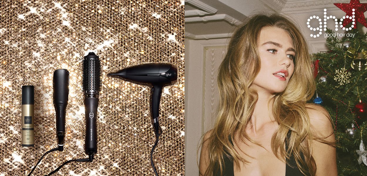 Haarstylingproducten zoals spray, stijltang, ronde borstel en föhn op een glinsterend gouden oppervlak naast een vrouw met gestyled golvend haar.