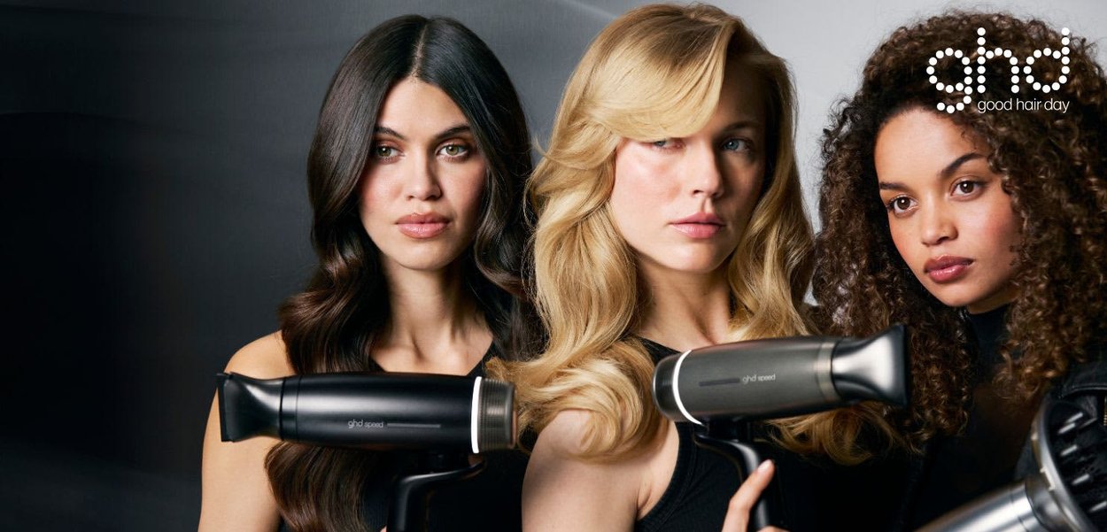Drie vrouwen met gestyled haar houden zwarte ghd-haardrogers vast en poseren tegen een donkere achtergrond met het ghd-logo in de hoek.