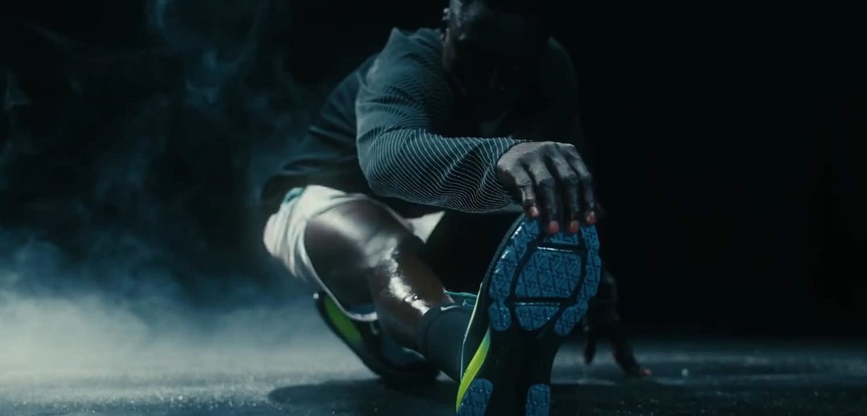 Sport Schuh mit einer strukturierten blauen Sohle und schwarz-grünen Akzenten. Der Fuß ist in einer Dehnung positioniert, wodurch der Schuh und das Design hervorgehoben werden.